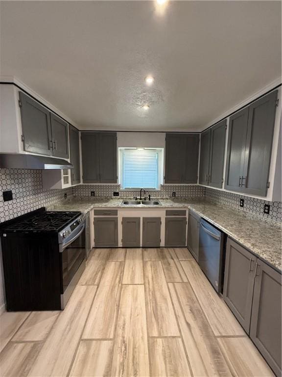 kitchen featuring stainless steel appliances, sink, backsplash, light stone counters, and light hardwood / wood-style flooring