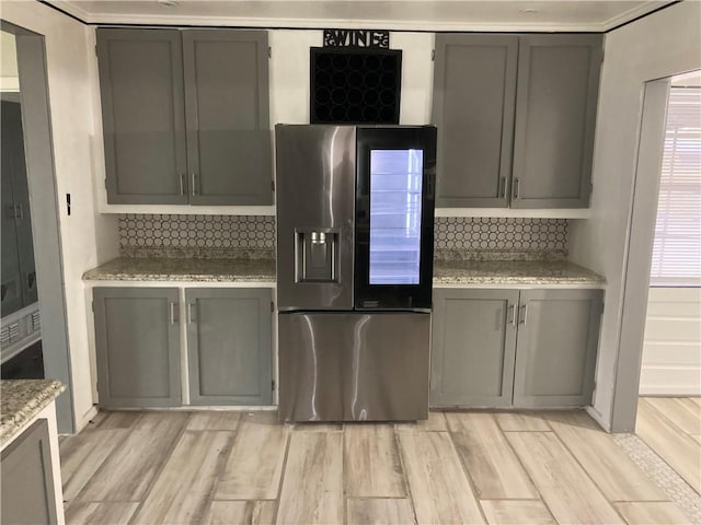 kitchen with gray cabinets, stainless steel fridge with ice dispenser, tasteful backsplash, and light wood-type flooring