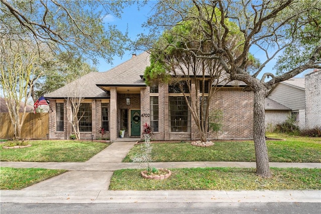 view of front of house with a front yard, brick siding, fence, and roof with shingles