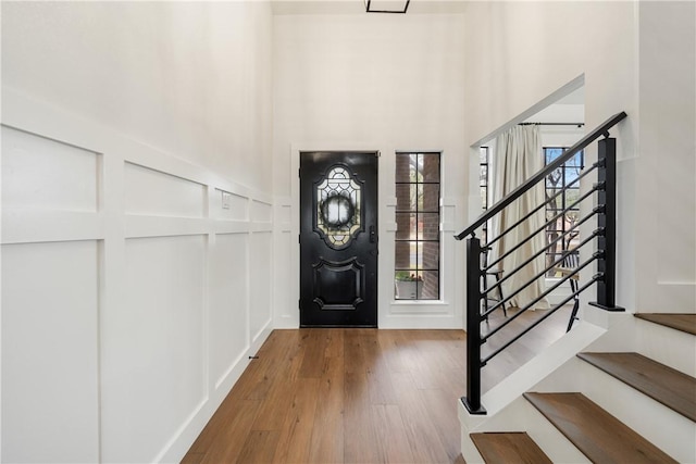 entrance foyer featuring a towering ceiling, stairs, a decorative wall, and wood finished floors