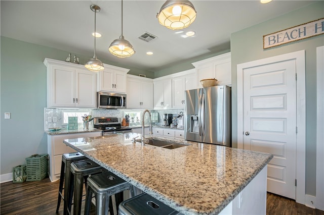 kitchen with white cabinets, stainless steel appliances, sink, and an island with sink