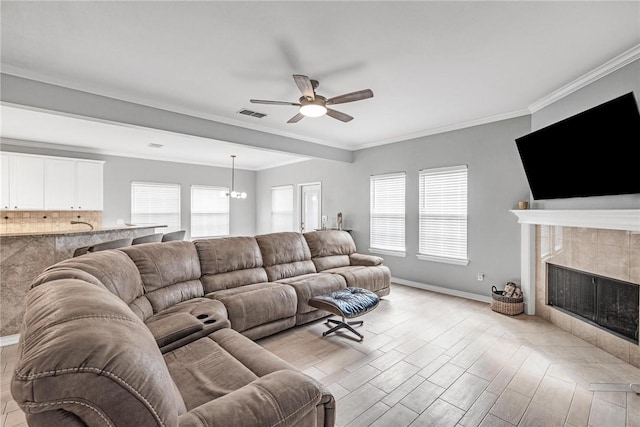 living room featuring a tile fireplace, light hardwood / wood-style floors, ceiling fan with notable chandelier, and ornamental molding