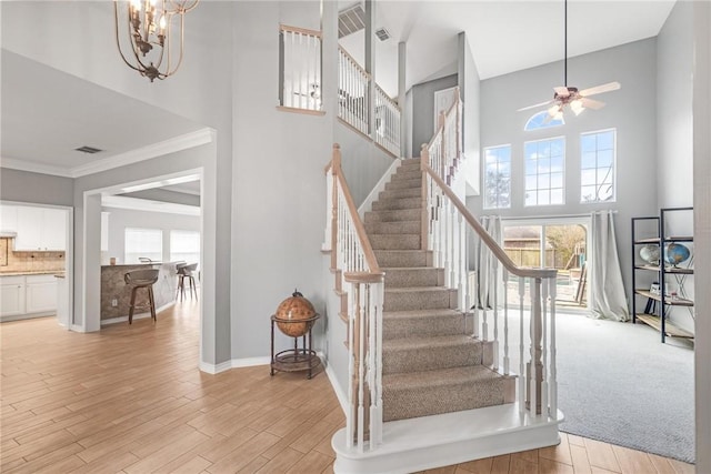 stairs with hardwood / wood-style flooring, ceiling fan with notable chandelier, crown molding, and a high ceiling