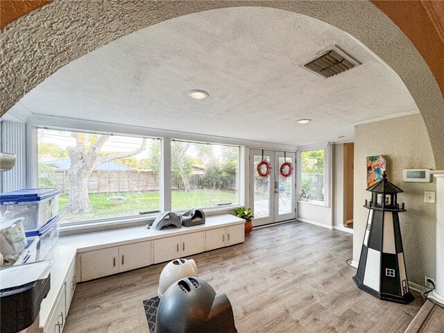 interior space with light wood-type flooring, a wealth of natural light, french doors, and a textured ceiling