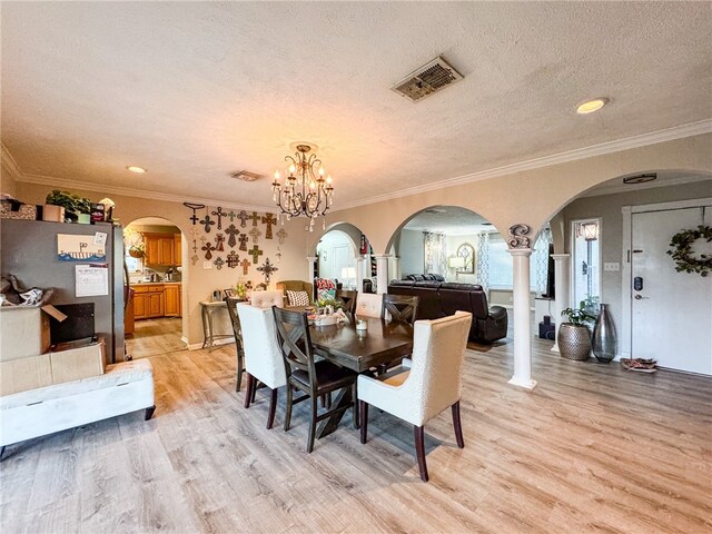 dining area featuring decorative columns, an inviting chandelier, crown molding, and light hardwood / wood-style flooring