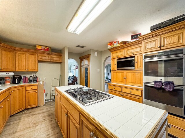 kitchen with stainless steel appliances, tile countertops, light hardwood / wood-style floors, a textured ceiling, and a kitchen island