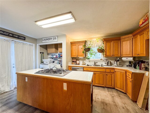 kitchen featuring stainless steel appliances, tile countertops, sink, a kitchen island, and light wood-type flooring