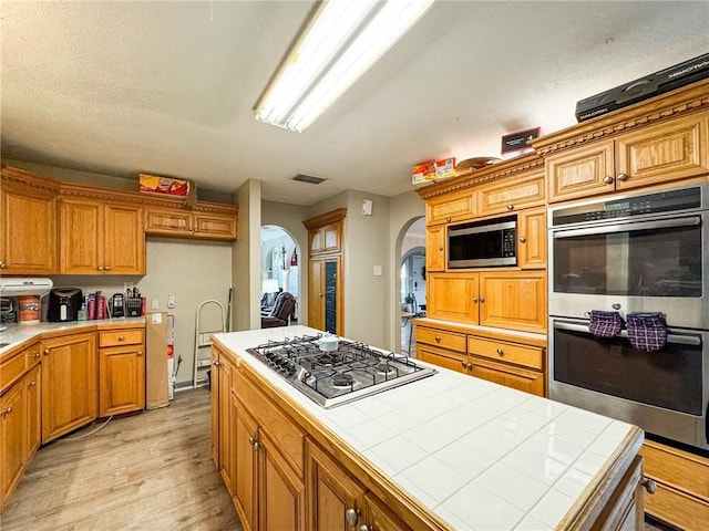 447 Santa Monica Pl, Corpus Christi, TX 78411 - kitchen with tile countertops, arched walkways, stainless steel appliances, light wood-style flooring, and brown cabinetry