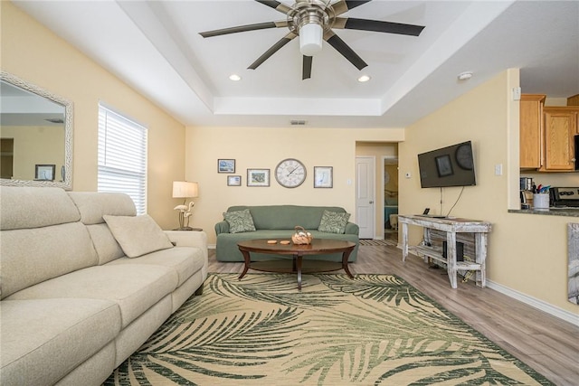 living room featuring ceiling fan, light hardwood / wood-style flooring, and a tray ceiling