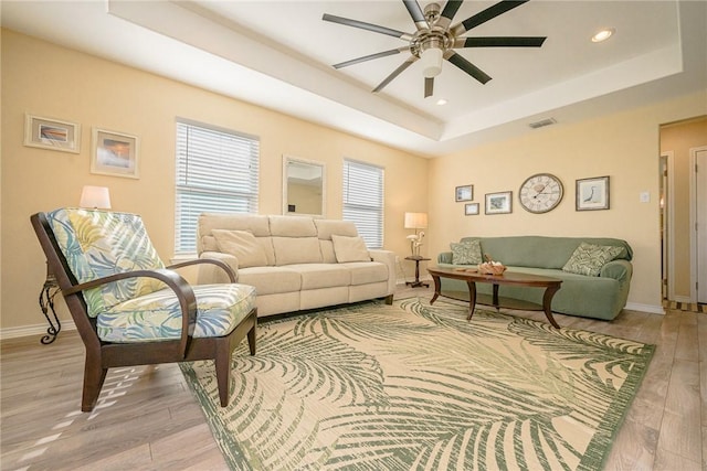 living room featuring a tray ceiling, ceiling fan, and light hardwood / wood-style floors