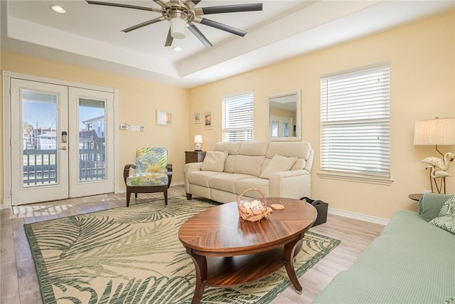 living room with a tray ceiling, ceiling fan, french doors, and light hardwood / wood-style floors