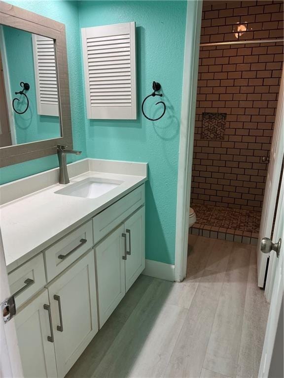 bathroom with tiled shower, vanity, hardwood / wood-style flooring, and toilet