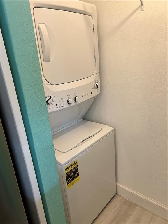 laundry room with stacked washer / dryer and light hardwood / wood-style floors