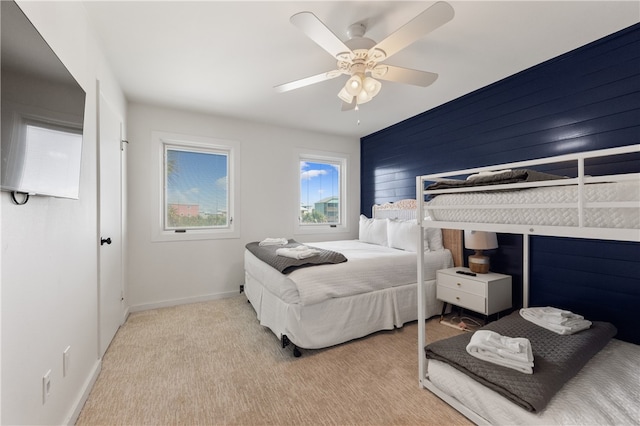 bedroom featuring ceiling fan, wooden walls, and light colored carpet