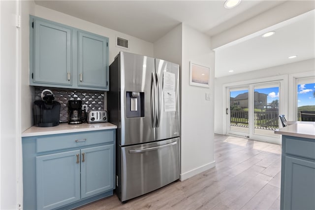 kitchen with tasteful backsplash, blue cabinets, stainless steel fridge, and light hardwood / wood-style flooring