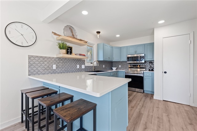 kitchen featuring stainless steel appliances, kitchen peninsula, a breakfast bar area, sink, and light hardwood / wood-style flooring