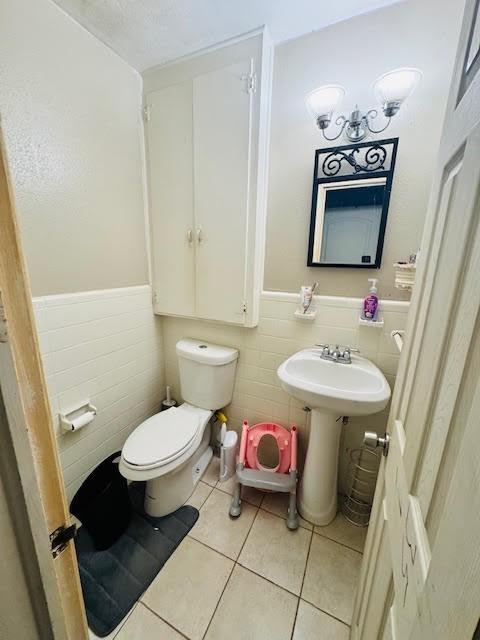 bathroom with toilet, tile walls, and tile patterned floors