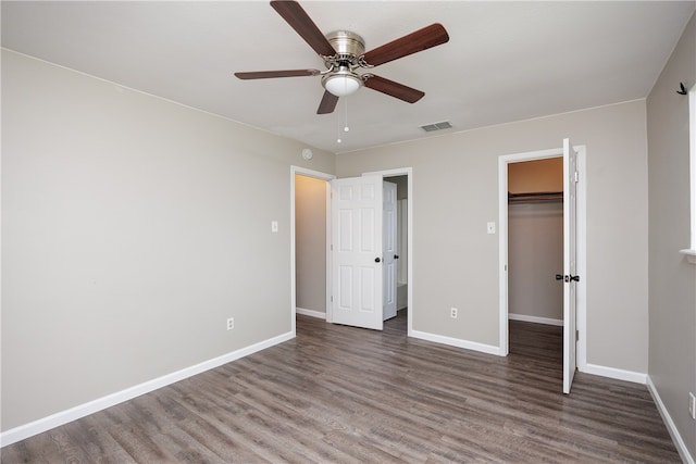 unfurnished bedroom with dark wood-type flooring, ceiling fan, a walk in closet, and a closet