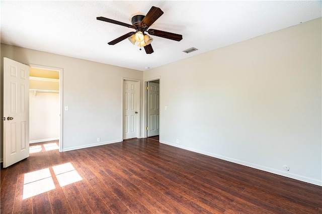 unfurnished bedroom with a spacious closet, ceiling fan, a closet, and dark hardwood / wood-style flooring