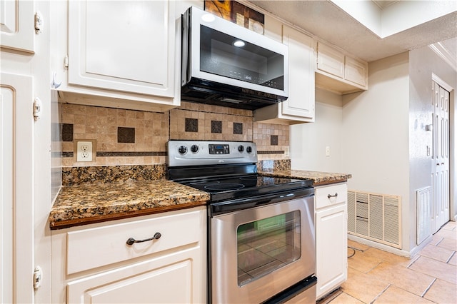 kitchen with stainless steel appliances, white cabinets, decorative backsplash, light tile patterned floors, and dark stone countertops