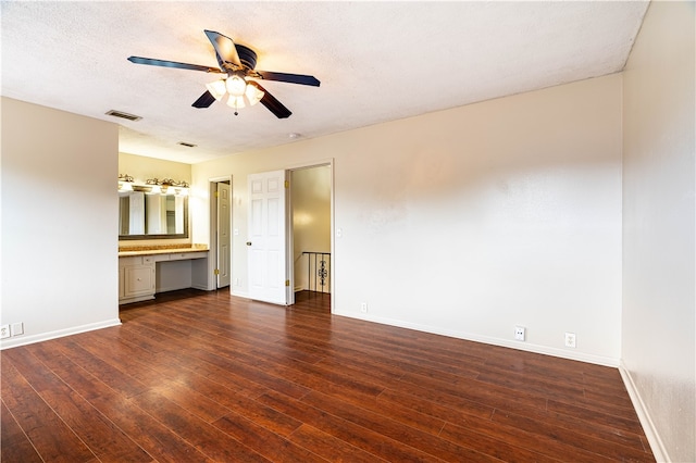 interior space featuring dark wood-type flooring, a textured ceiling, built in desk, and ceiling fan