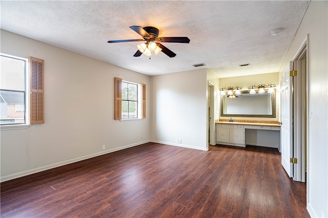 unfurnished bedroom featuring dark hardwood / wood-style flooring, a textured ceiling, built in desk, and ceiling fan