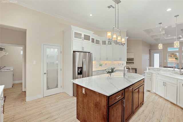 kitchen with a center island with sink, sink, tasteful backsplash, hanging light fixtures, and light wood-type flooring