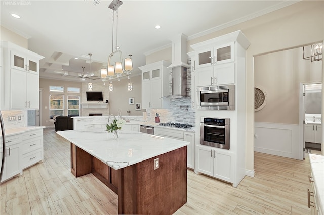 kitchen featuring white cabinets, crown molding, a kitchen island, appliances with stainless steel finishes, and decorative light fixtures