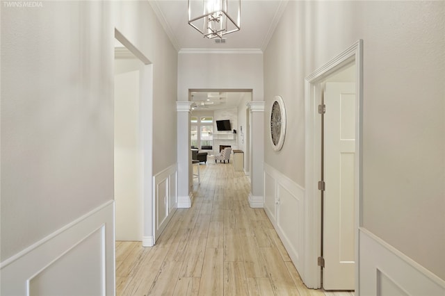 hallway with ornamental molding, light hardwood / wood-style flooring, decorative columns, and an inviting chandelier