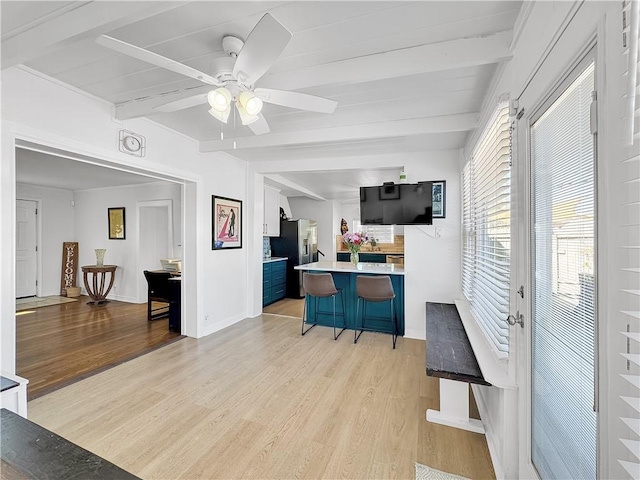 kitchen featuring stainless steel fridge, light wood-style flooring, a breakfast bar area, beamed ceiling, and light countertops