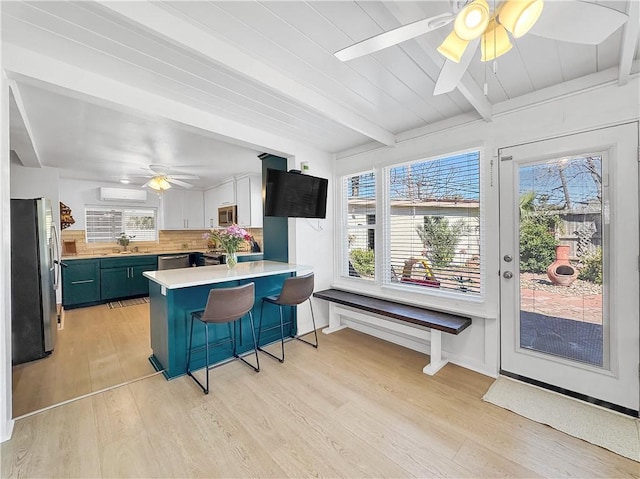 kitchen featuring a peninsula, a sink, stainless steel appliances, light wood-type flooring, and beam ceiling