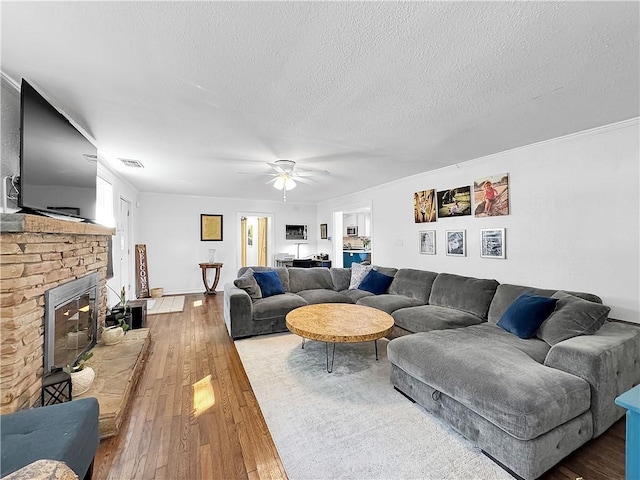 living area with visible vents, a ceiling fan, a brick fireplace, a textured ceiling, and hardwood / wood-style floors