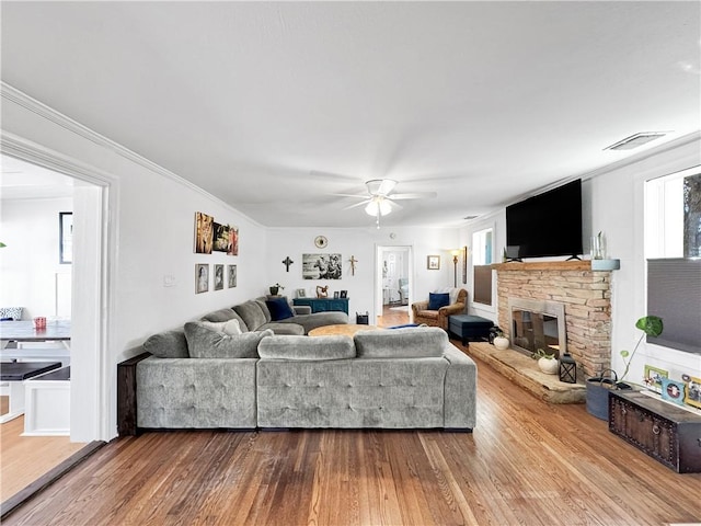 living room with visible vents, dark wood finished floors, a ceiling fan, ornamental molding, and a fireplace