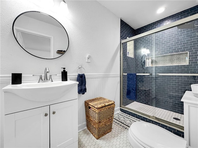 full bathroom featuring toilet, a wainscoted wall, tile patterned flooring, vanity, and a shower stall