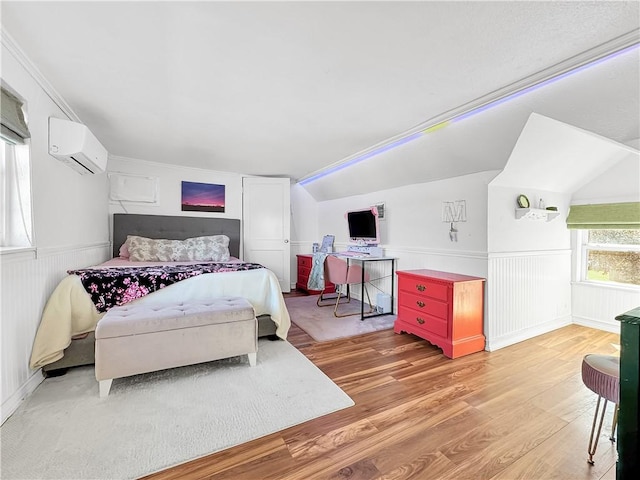 bedroom with light wood-style floors, a wainscoted wall, a wall mounted air conditioner, and vaulted ceiling