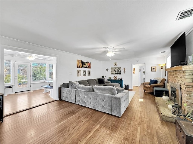 living area with light wood-style floors, ceiling fan, a fireplace, and visible vents