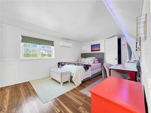 bedroom with wainscoting, a textured ceiling, wood finished floors, and a wall mounted AC