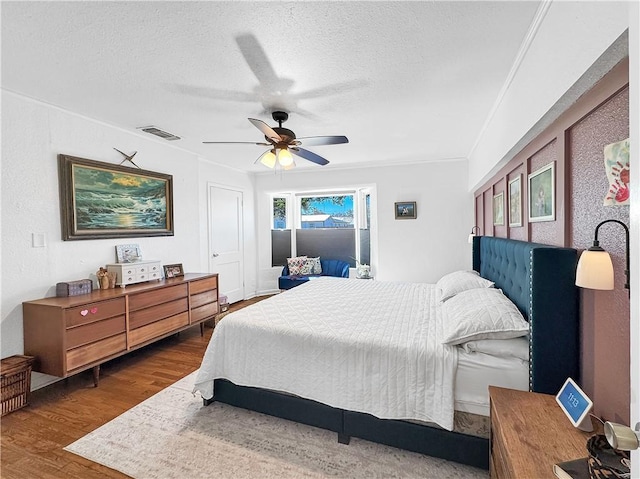 bedroom with visible vents, a ceiling fan, wood finished floors, crown molding, and a textured ceiling