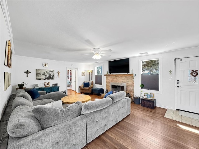 living area featuring visible vents, plenty of natural light, a stone fireplace, and wood finished floors