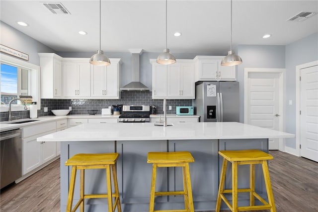 kitchen with wall chimney range hood, stainless steel appliances, and a kitchen island