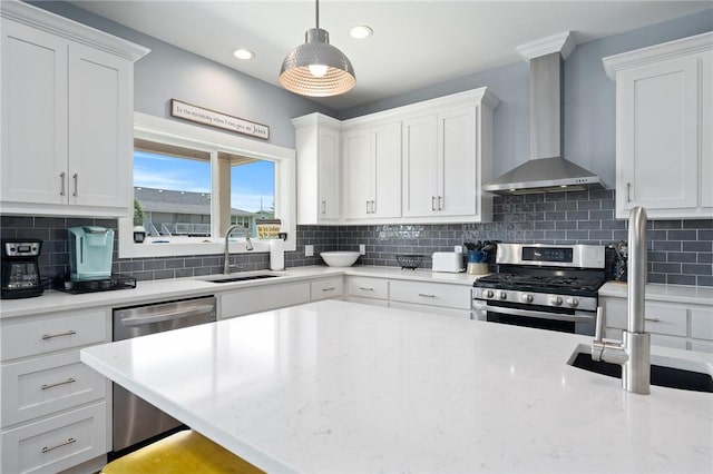 kitchen with appliances with stainless steel finishes, white cabinetry, sink, hanging light fixtures, and wall chimney exhaust hood