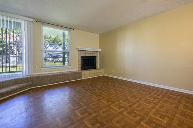 unfurnished living room featuring dark parquet floors, a textured ceiling, and a tiled fireplace