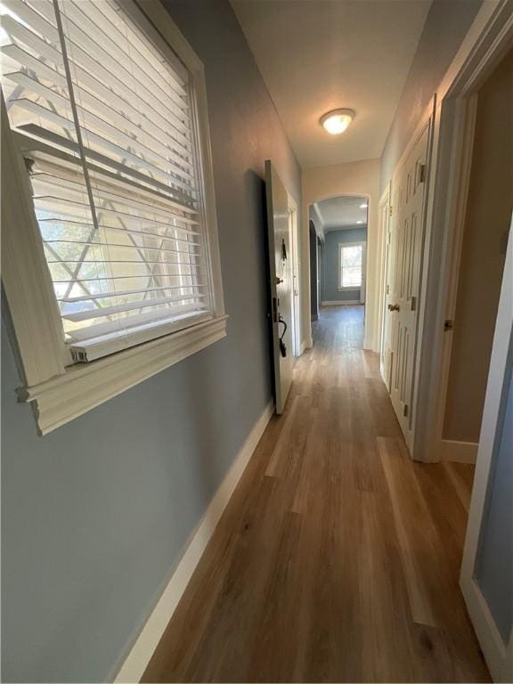 corridor featuring arched walkways, baseboards, and wood finished floors