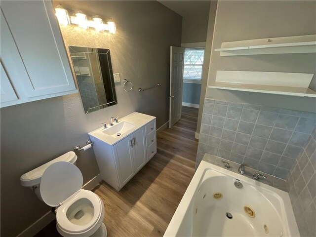 bathroom with baseboards, tiled tub, toilet, wood finished floors, and vanity