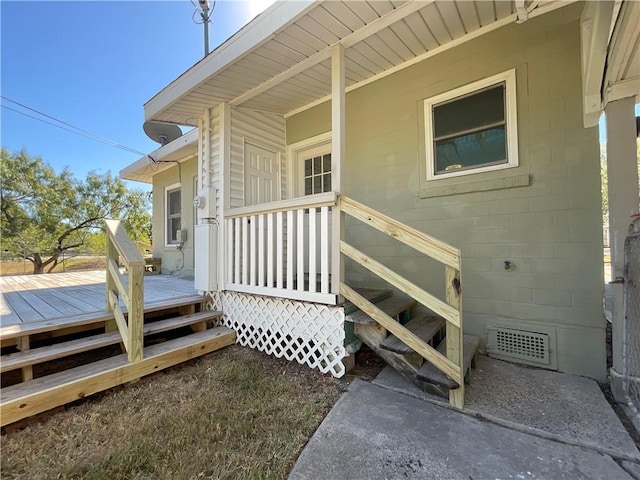 view of exterior entry featuring a deck, concrete block siding, and visible vents