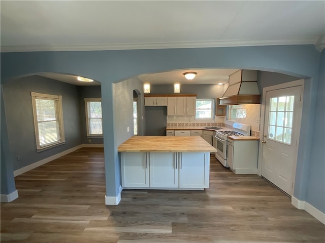 kitchen featuring arched walkways, butcher block counters, custom range hood, and white gas range oven