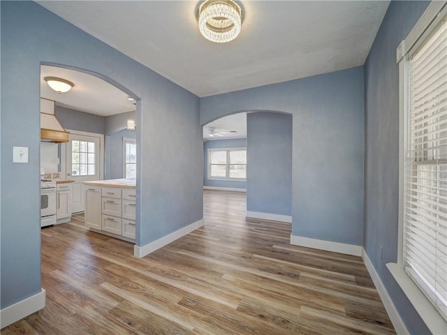 interior space with baseboards, arched walkways, and light wood finished floors