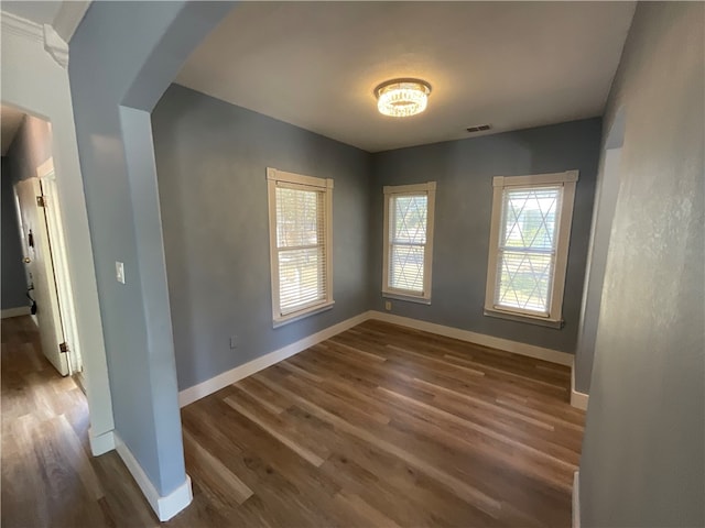 empty room featuring visible vents, arched walkways, baseboards, and wood finished floors