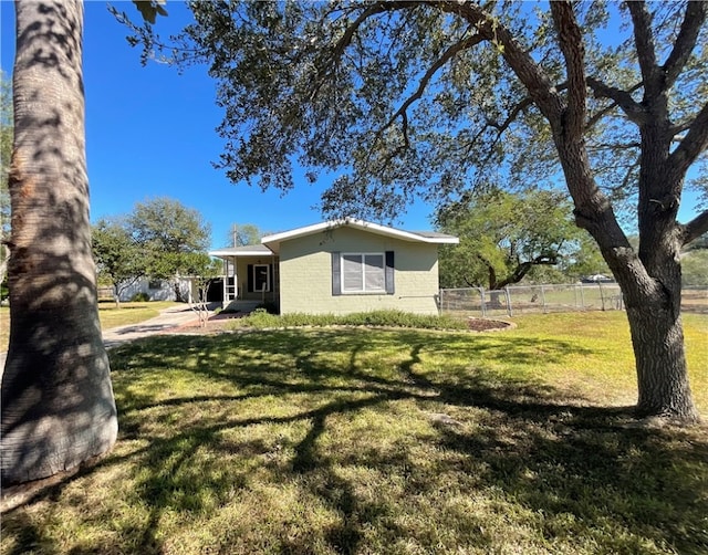 exterior space featuring concrete block siding, a front lawn, and fence