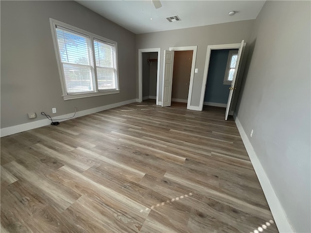 unfurnished bedroom featuring multiple windows, two closets, light wood-style flooring, and baseboards